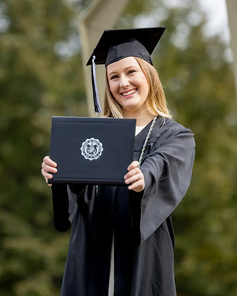 A student in cap and gown holds a diploma