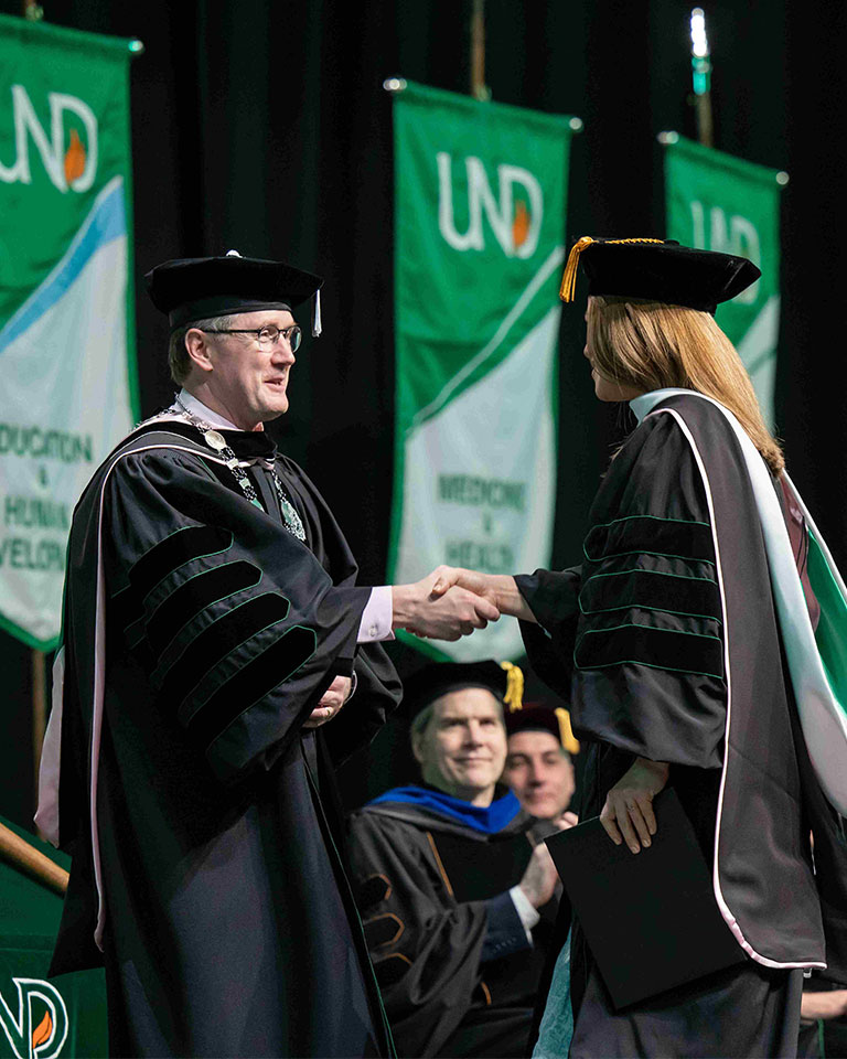 und president shaking someone's hand at graduation 