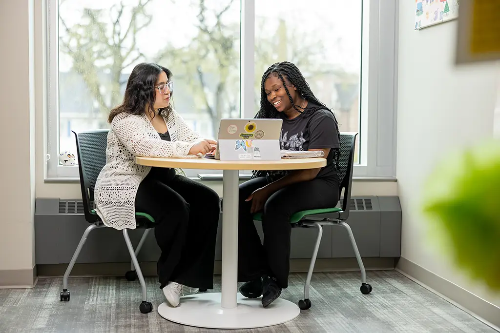 Two women talking at a round table with a laptop