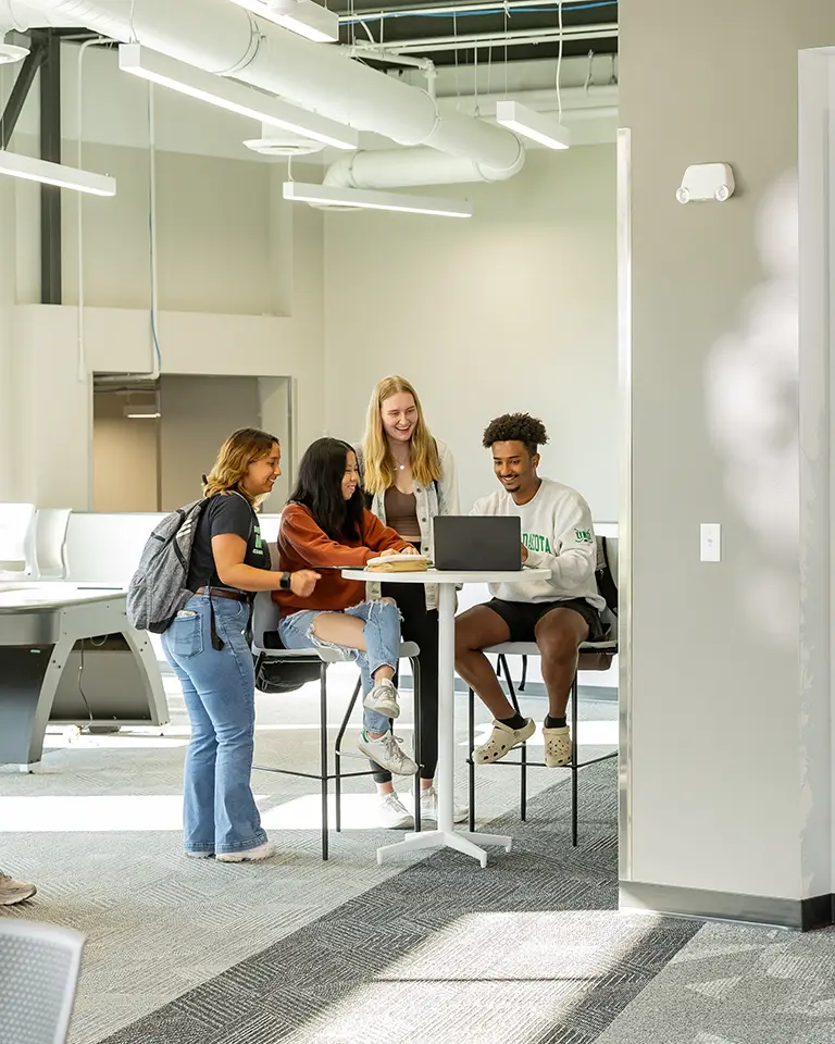 Four students looking a laptop on a high top table