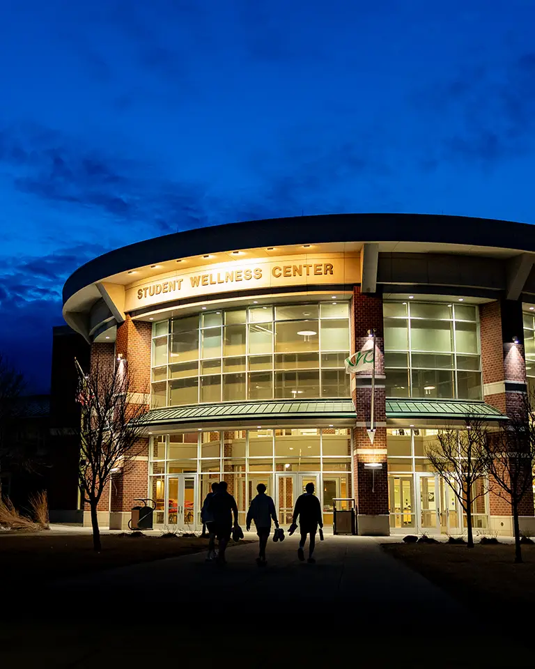 three students walking into the Wellness Center at dusk