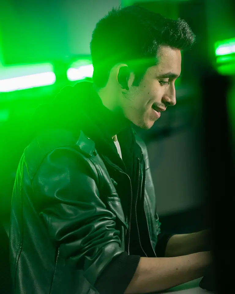 student on computer with green lights behind his head