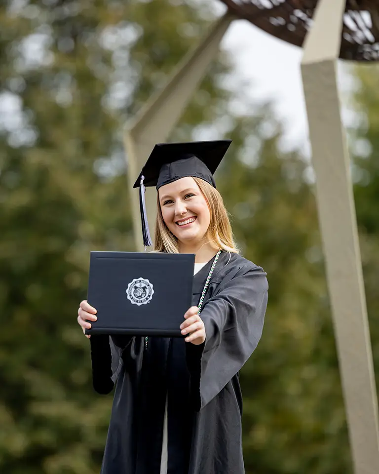 A student in cap and gown holds a diploma
