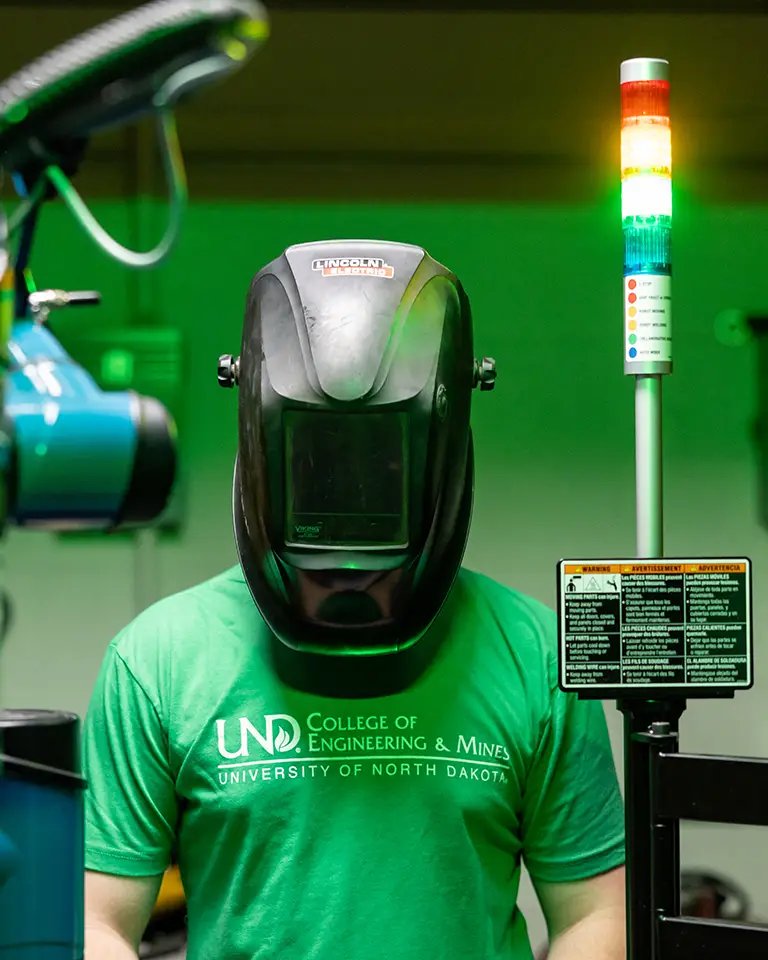 A student in a welding mask waits for an experiment to finish.