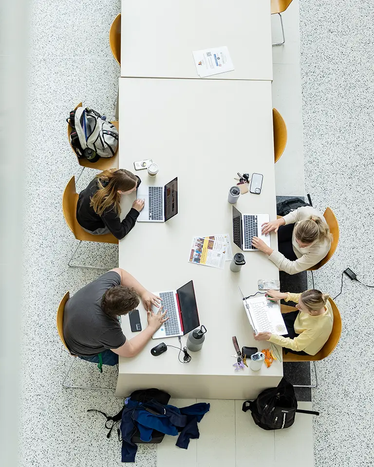 A view of above of four students studying at a table with open laptops.