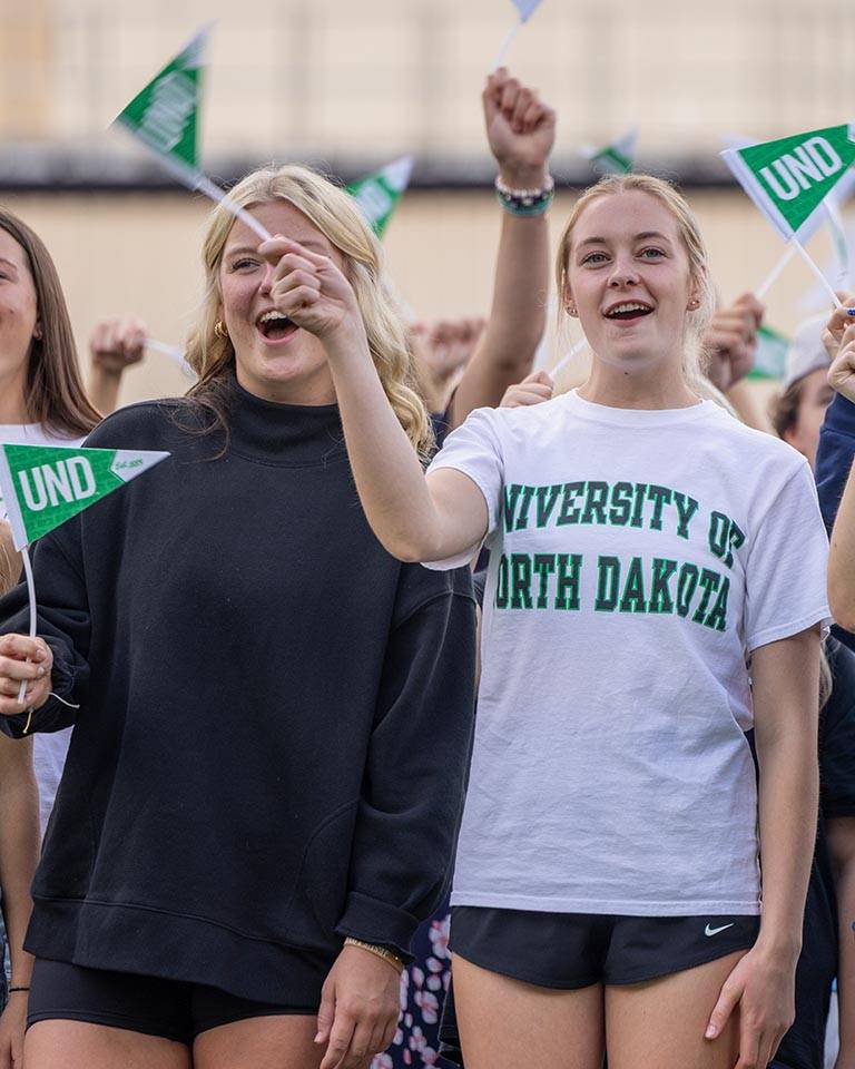 Two students smiling and waving flags