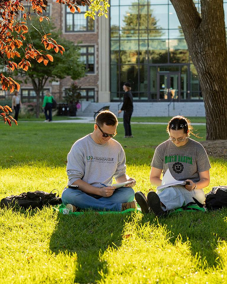 Two students study in the grass in front in the campus quad.