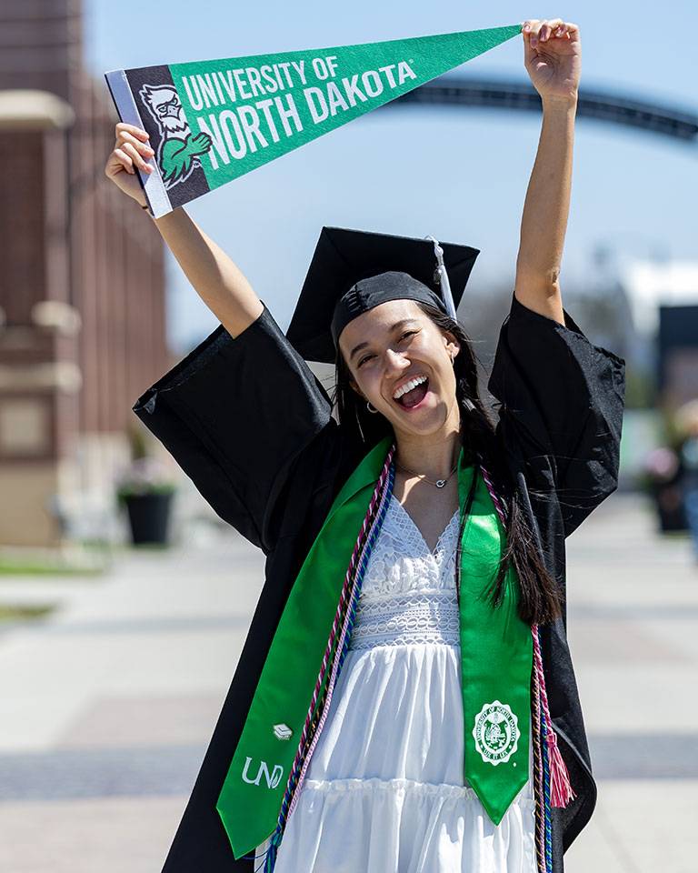 A student in Commencement cap and gown holds a pennant.