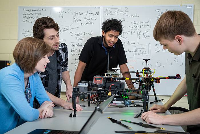 Four students pointing at a drone