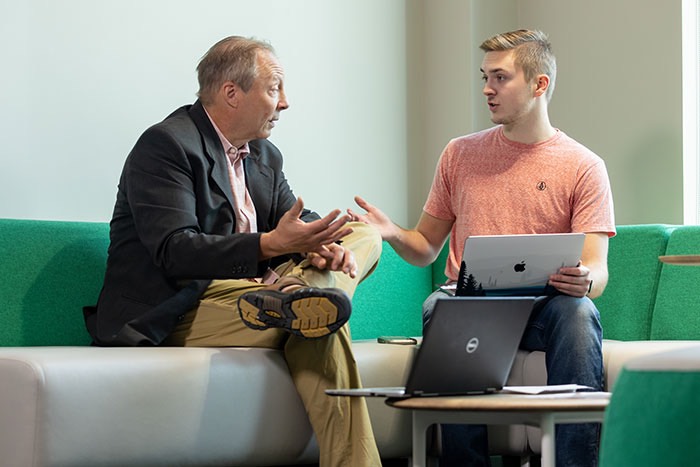 professor talking to student on couch with two laptops