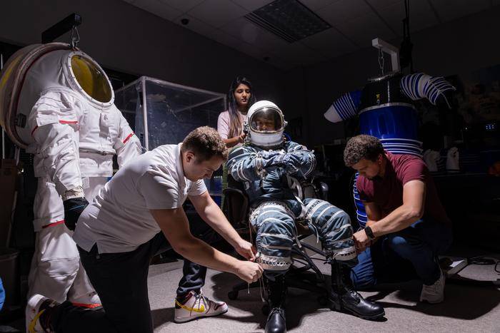 three students putting one student in space suit