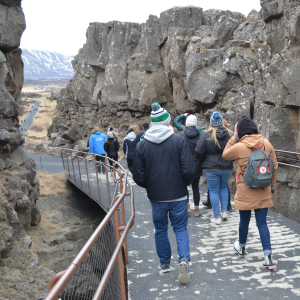 A group of UND students walking away from the camera down a path cut between tall rock-face.