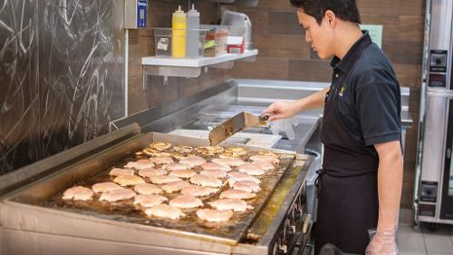 Dining Services student worker manages a flat top grill cooking several servings of boneless, skinless chicken breast