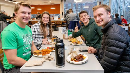 4 students share a table in the Dining Center and smile for the camera at the Super Bowl Party theme meal 2026
