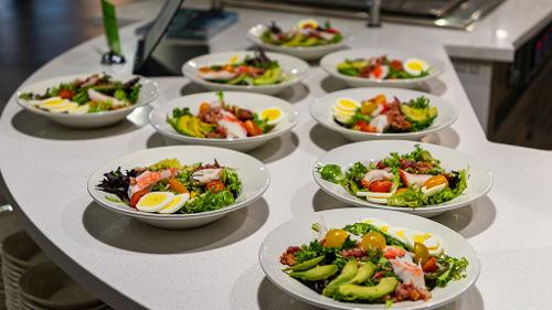 Individual bowls of leafy green salad with crab meat sit on a counter to be picked up by students