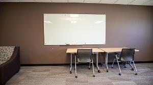 whiteboard attached to a wall with table and chair beneath it