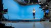 Meteorology student gives weather report in front of blue screen 
