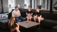 Four young people playing a game of cards in a lounge space with a large table and sectional sofa