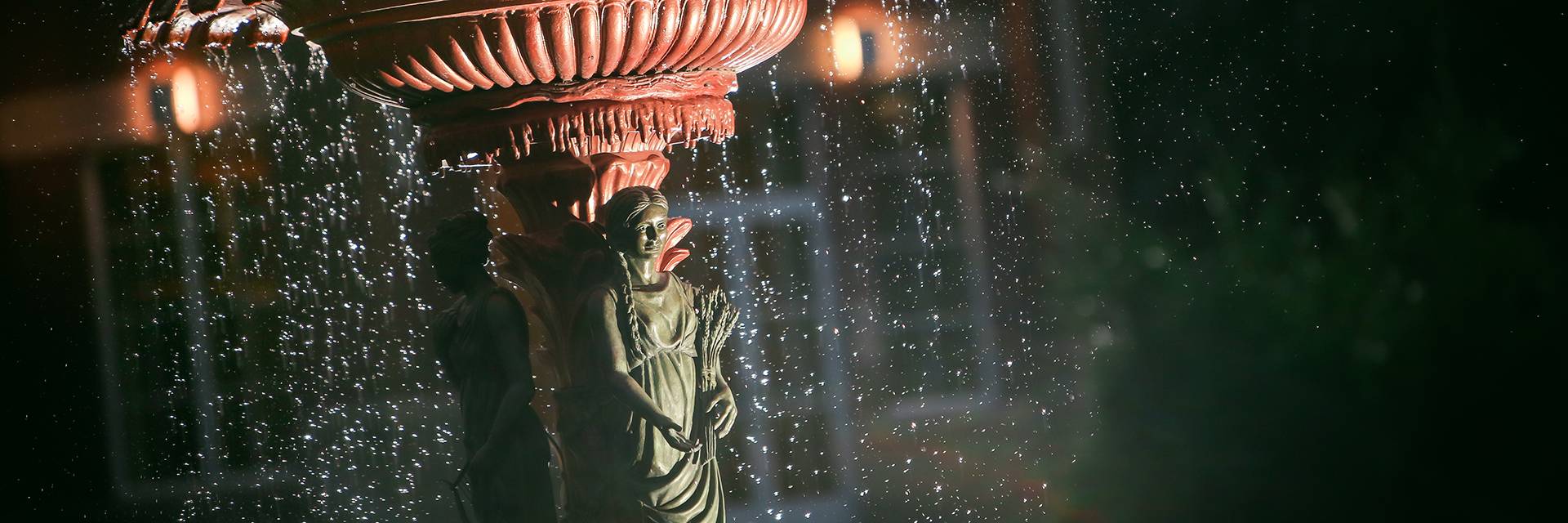 The Adelphi Fountain at UND, featuring a bronze figure against the red center pedestal, water droplets falling around the figure