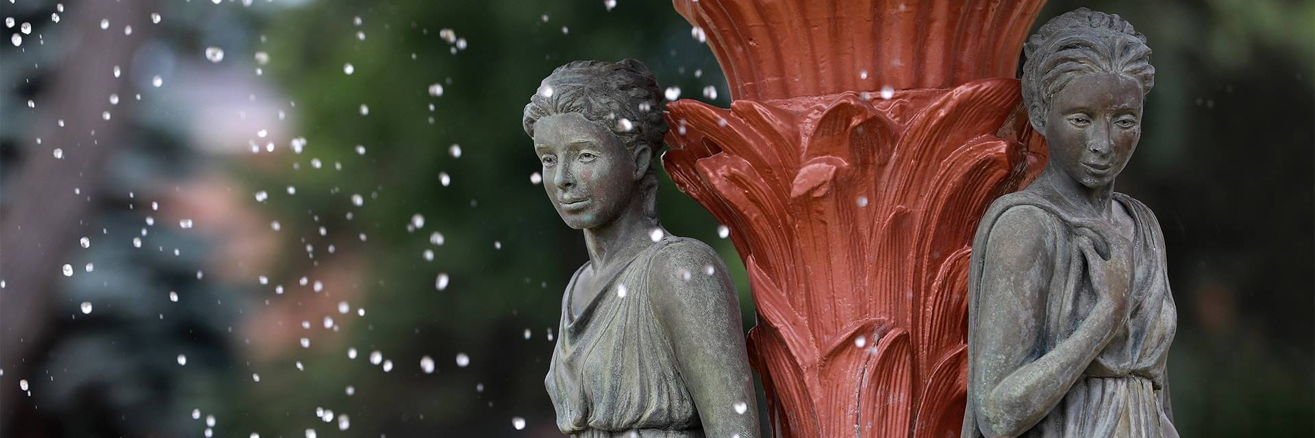 The Adelphi Fountain at UND, featuring a bronze figure against the red center pedestal, water droplets falling around the figure