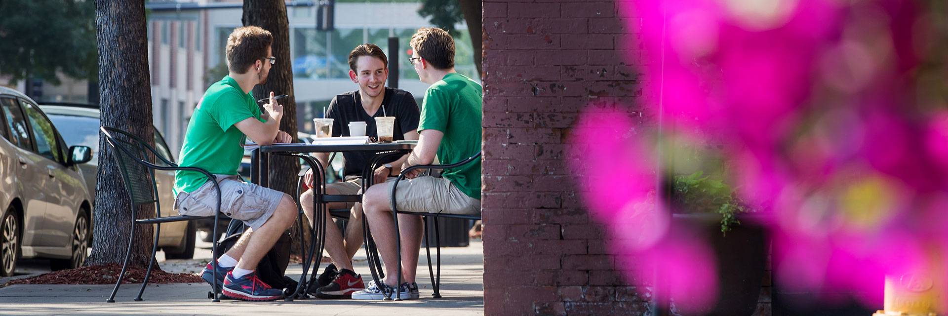 three students sit at a table while drinking coffee.