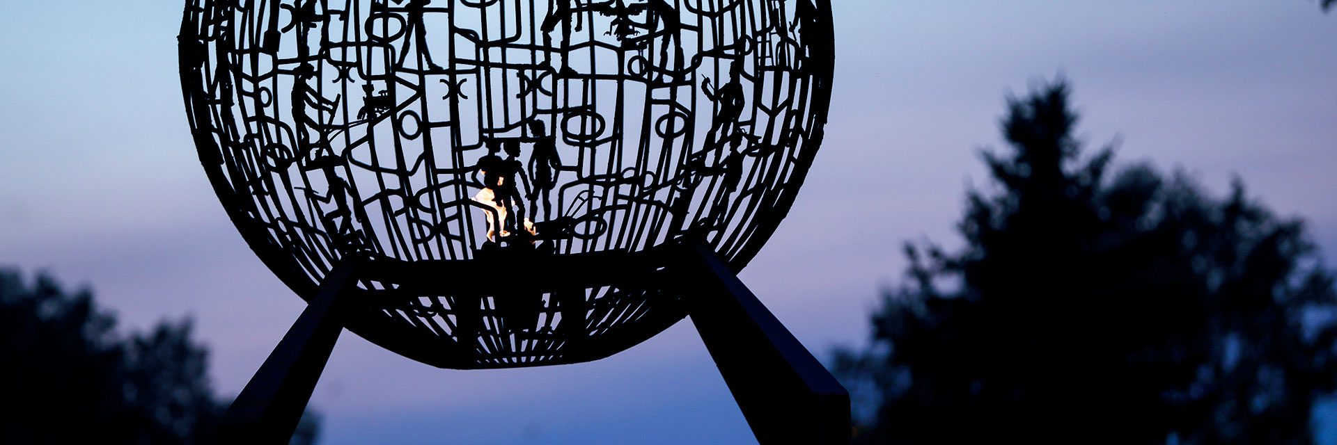 View of sky looking through spherical sculpture containing a flame within the sphere, located on UND's campus