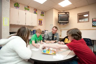 a teacher seated at a table with students with special needs, actively engaging in learning together