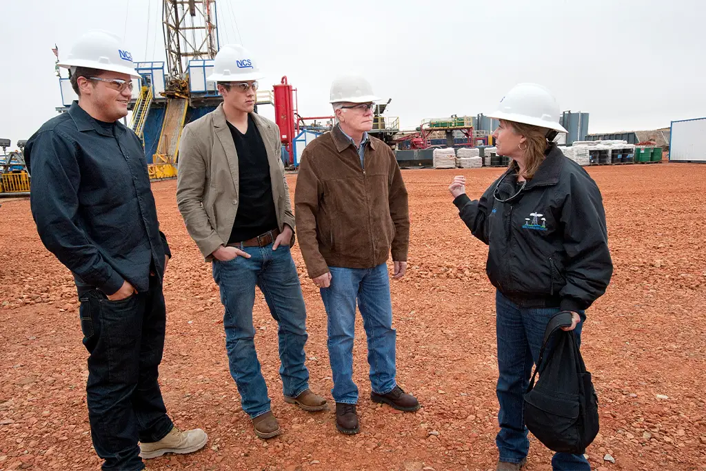 A team of engineers discusses a project at an industrial field site, highlighting the real-world application of knowledge and professional development that are essential steps on the path to earning a PE license.