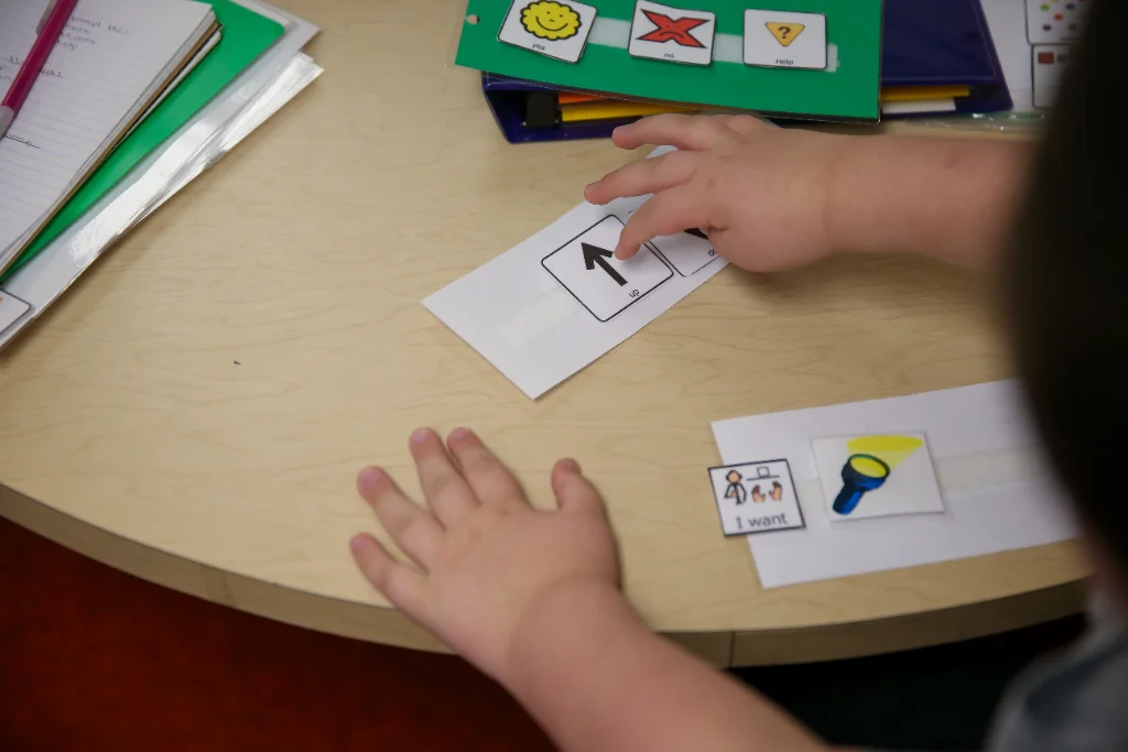 A child's hands interact with educational cards on a wooden table, displaying symbols and illustrations for teaching concepts