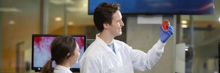  A medical laboratory science student smiles while holding a culture plate up to examine the growth on it.