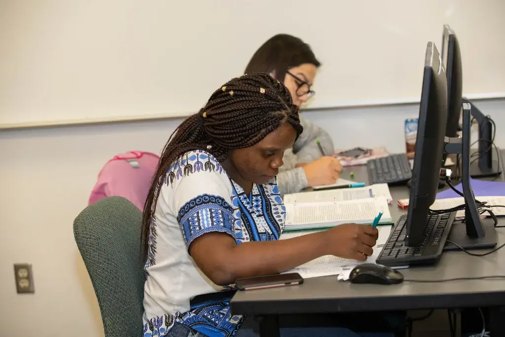 Two students are working on computers in a classroom, learning computer science.