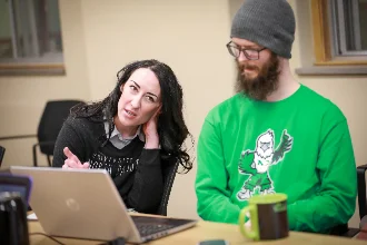 Two psychology students discuss coursework while looking at a laptop.