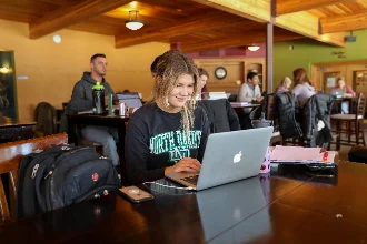 A female data science student seated in the campus cafeteria, focused as she searches for data science resources on her laptop