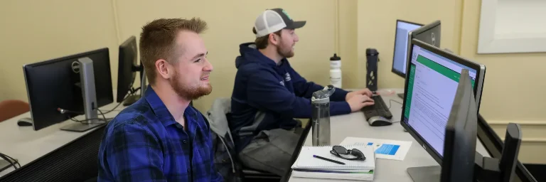 Two data analytics students are in a computer lab, smiling as they take an online exam