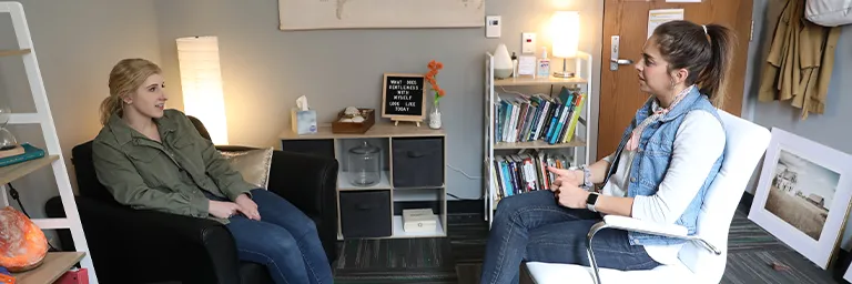A counselor and a student talk while seated in a warmly decorated counseling office.