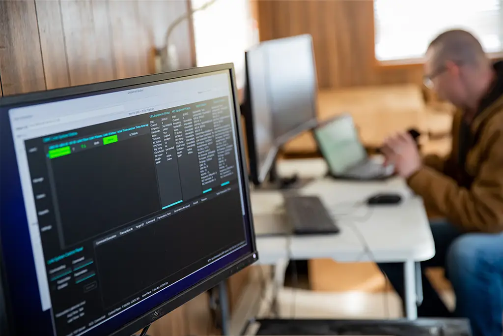 Computer screen showing coded data and system details in focus, while a professional works at a desk in the background, symbolizing secure data management and ethical handling of information in AI