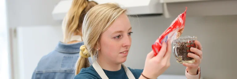 A nutrition student measures chocolate chips in a measuring cup, carefully observing the portion size