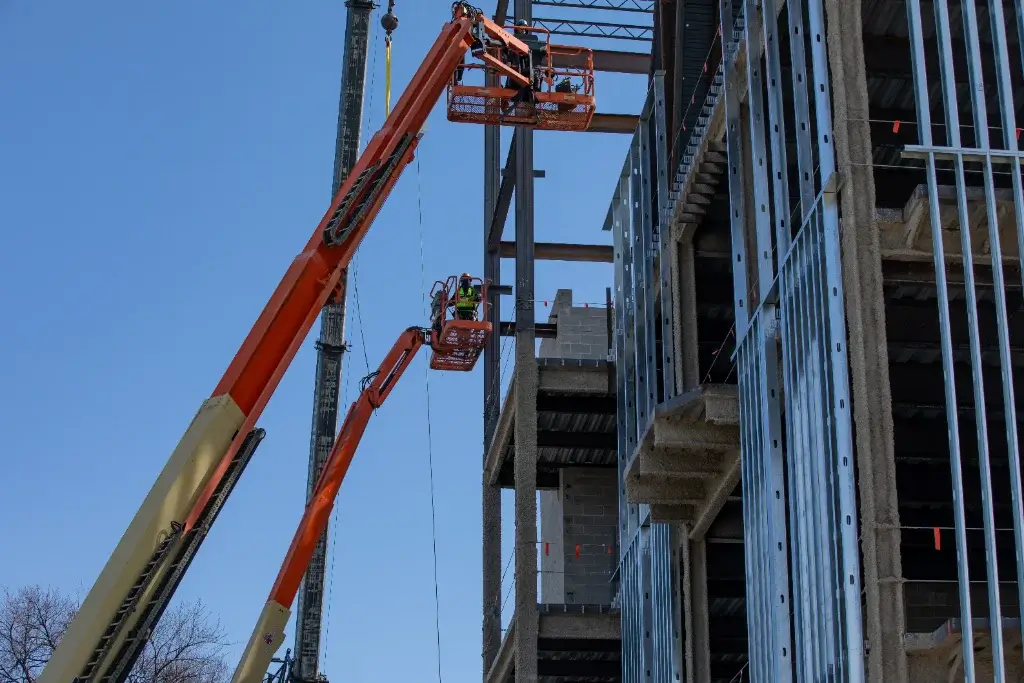 A construction site with a large orange crane and a worker on an extended cherry picker platform