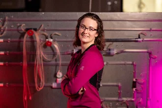 A female chemical engineering student sitting at a lab bench, posing for a picture with a confident smile