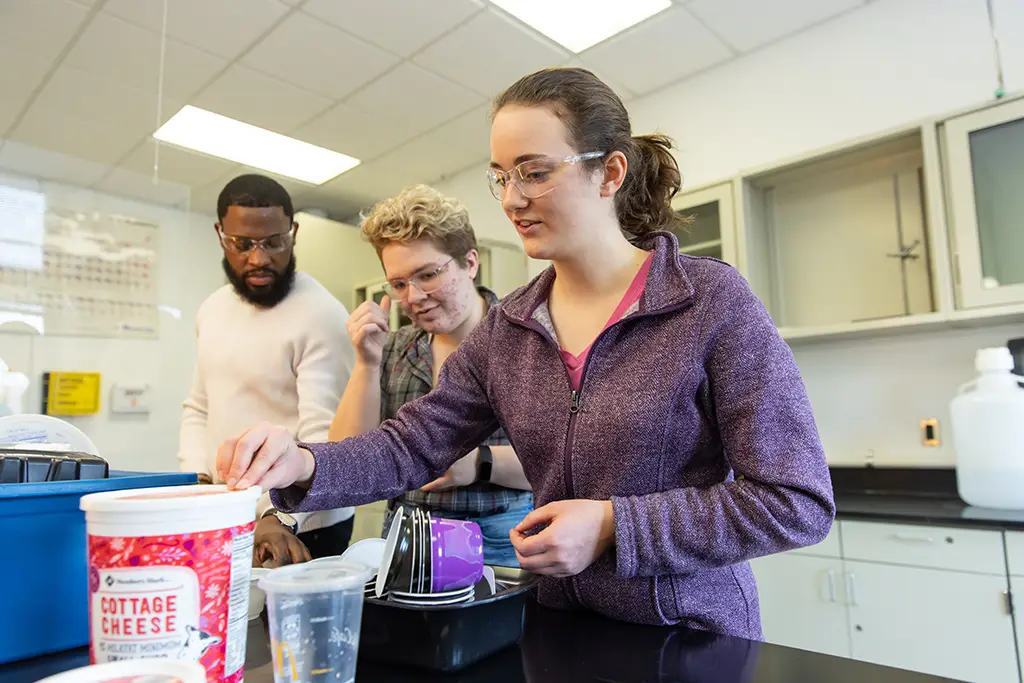 Three chemical engineering students wearing safety goggles while conducting food science experiment in the university lab.