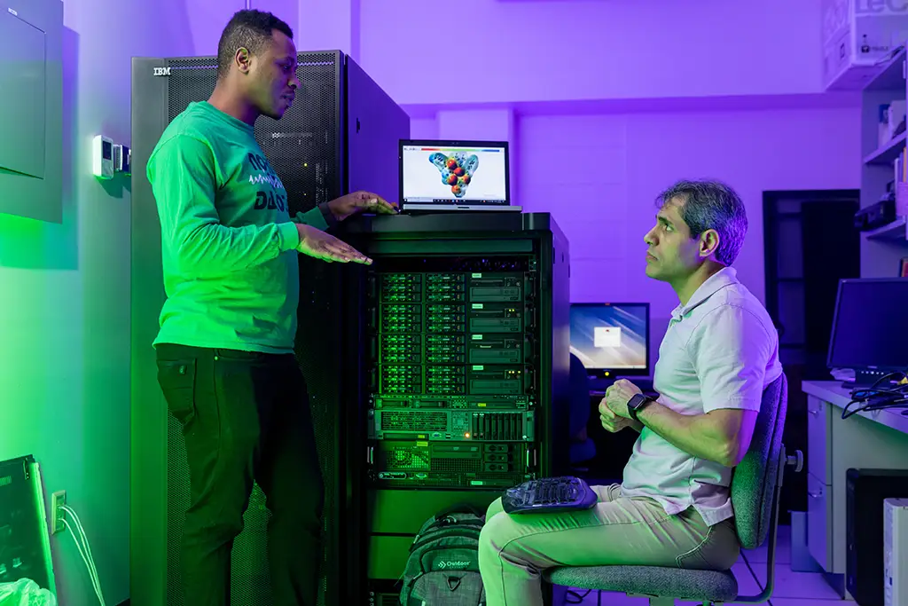 Two researchers illustrating their dependency on data by analyzing a complex 3D model on a laptop connected to a high-performance IBM server.
