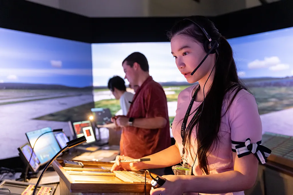 A student in a headset marks flight progress strips while operating the tower simulator.