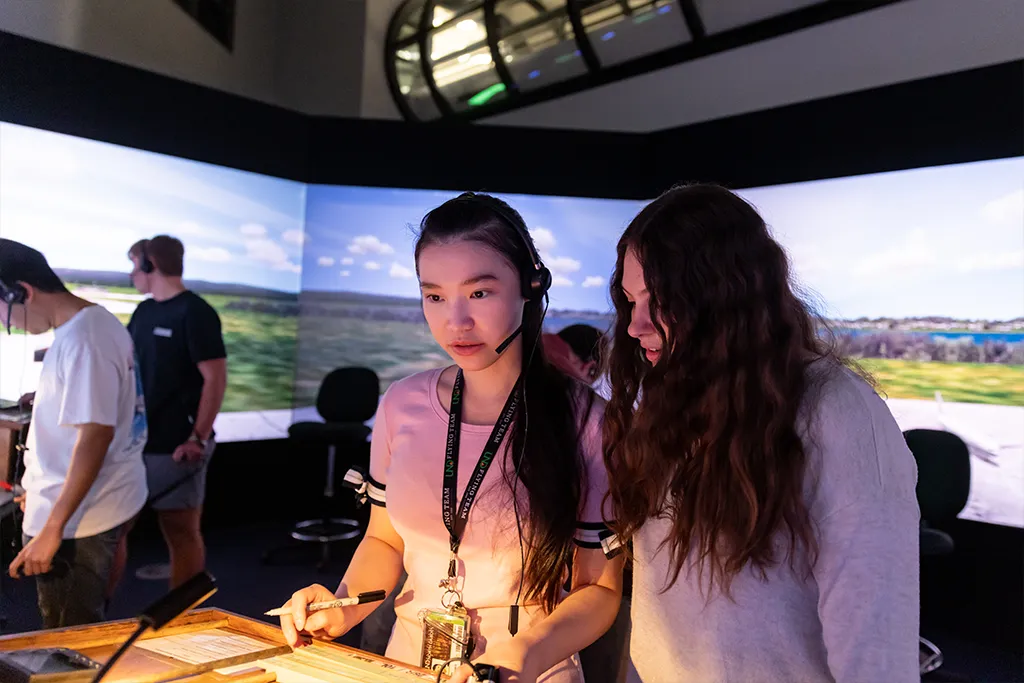 Two air traffic control students in headsets confer over flight strips in the tower simulator.