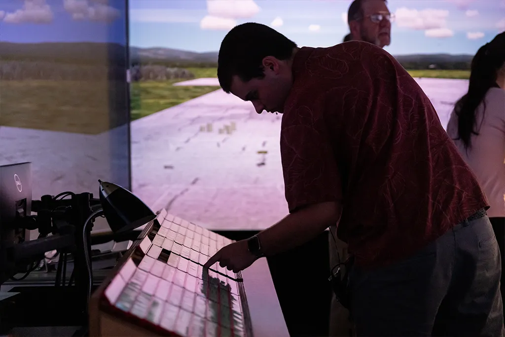 An air traffic control student works a control panel in front of the runway screens of a tower simulator.