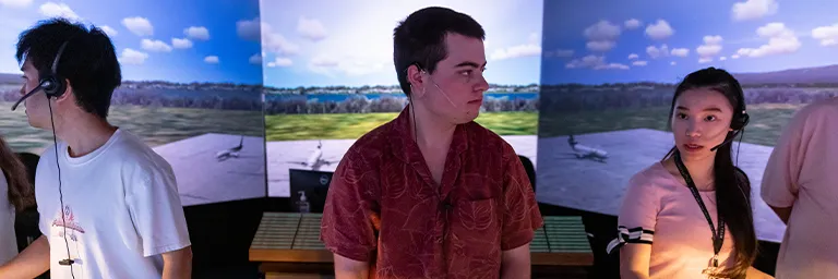 Three air traffic control students wearing headsets stand in the panoramic tower simulator.