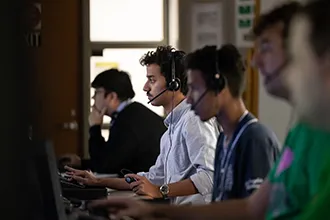 A row of air traffic control students wearing headsets work at radar consoles in a darkened lab.