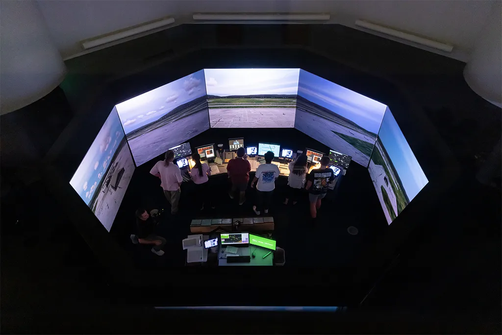Overhead view of students staffing stations inside the 360-degree tower simulator with runway screens.