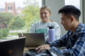 Two students smiling while working on laptops