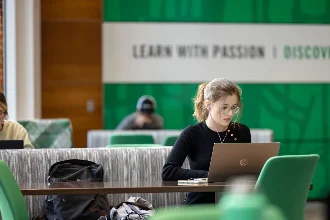 A female student seated on campus with a laptop