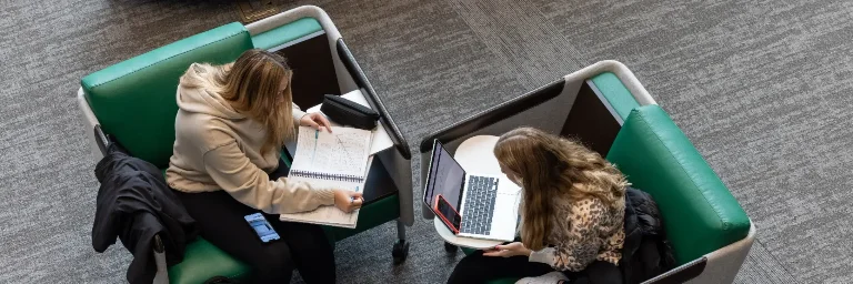  Two students seated at a table, each engrossed in their homework, captured from a high perspective